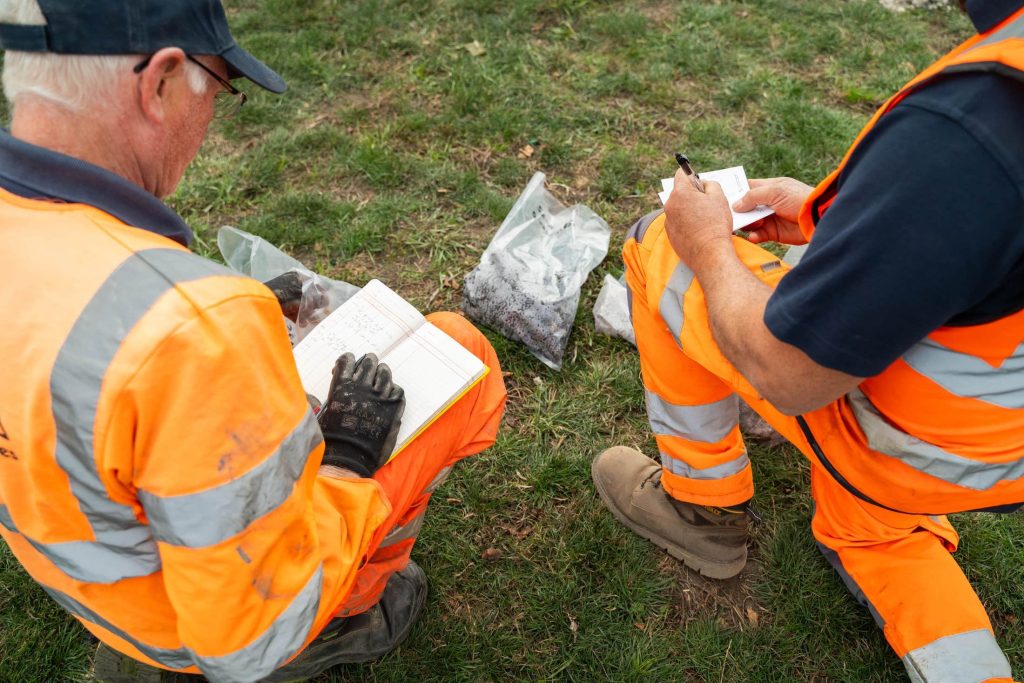 Engineers recording soil data during window sampling ground investigation on grassed site